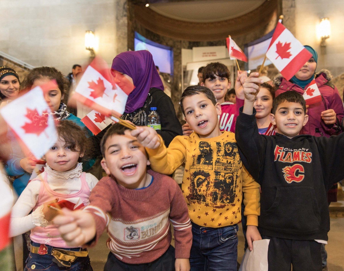 A group of Syrian children smile and wave Canadian flags in front of the ROMâs Schad Gallery of Biodiversity
